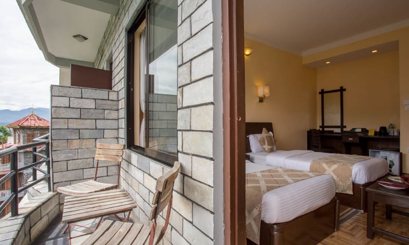Deluxe room with a stone-walled balcony, two chairs and twin beds visible through the open door