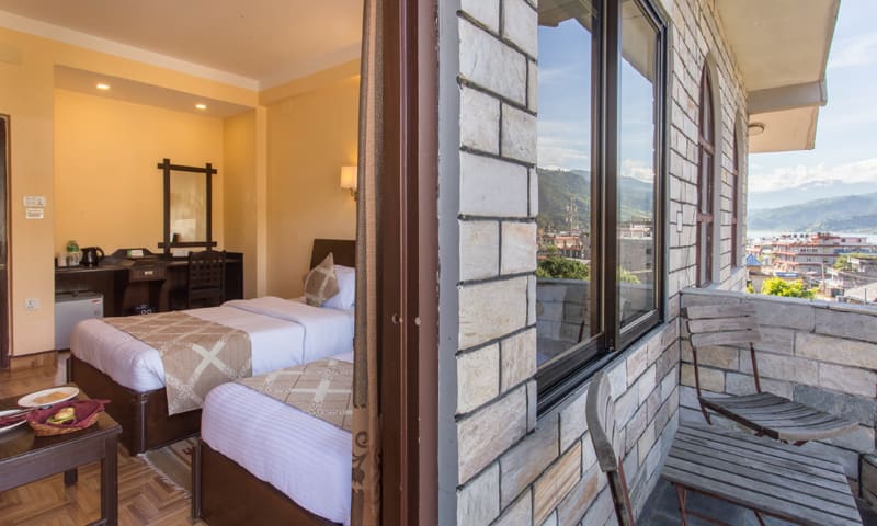 Twin beds beside an open balcony door with views over Pokhara