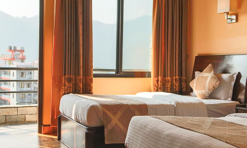 Deluxe room corner with tall windows, warm curtains and twin beds
