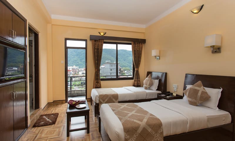 Deluxe room with twin beds, wooden furniture and a window onto green hills