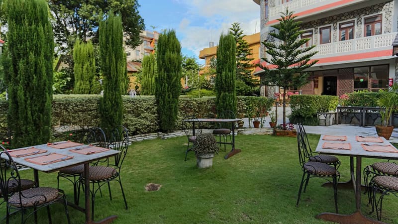 Wrought-iron tables on the garden lawn, with cypress trees and the hotel buildings behind
