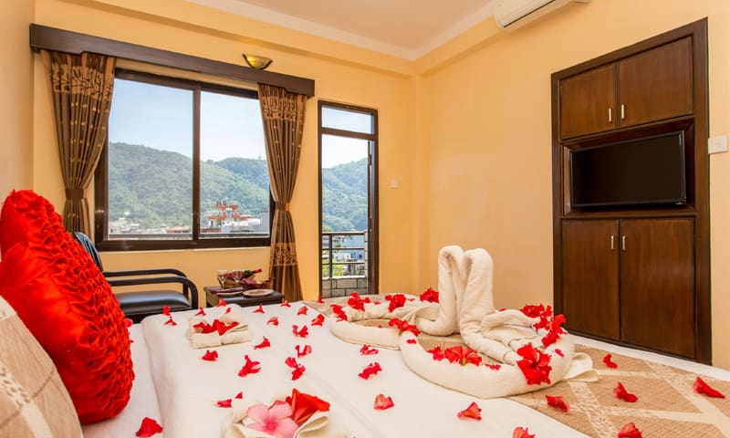 The Honeymoon Super Deluxe with petals on the bed and a window onto hills