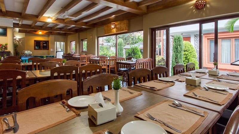 The restaurant’s timber-beamed dining room with set tables and tall windows onto the garden