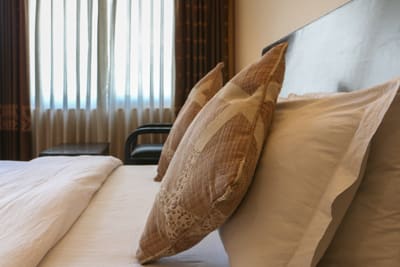 Patterned cushions on a made bed beside a window with sheer curtains