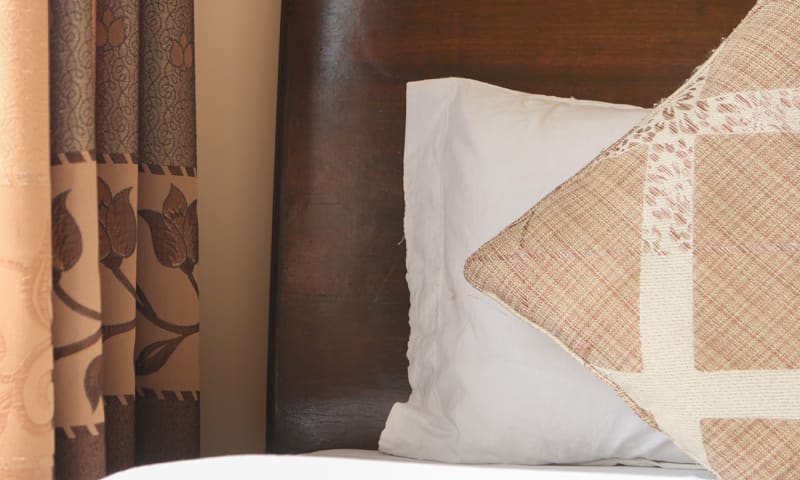 Close view of pillows and a patterned cushion against a wooden headboard